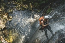 A man canyoning down a steep rock face towards water.